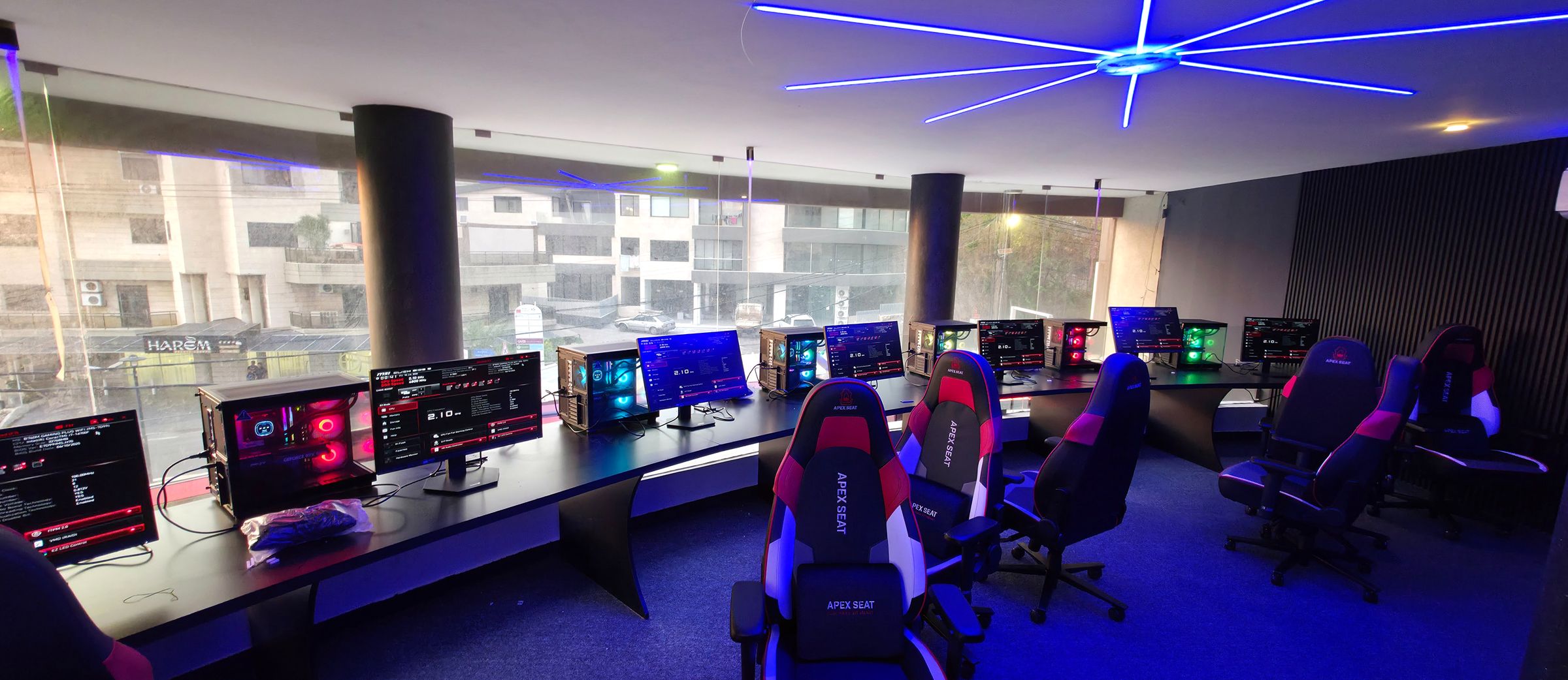 Gaming lounge built by LuxeSetups, with a curved desk of illuminated PCs and racing seats beneath a blue starburst light fixture